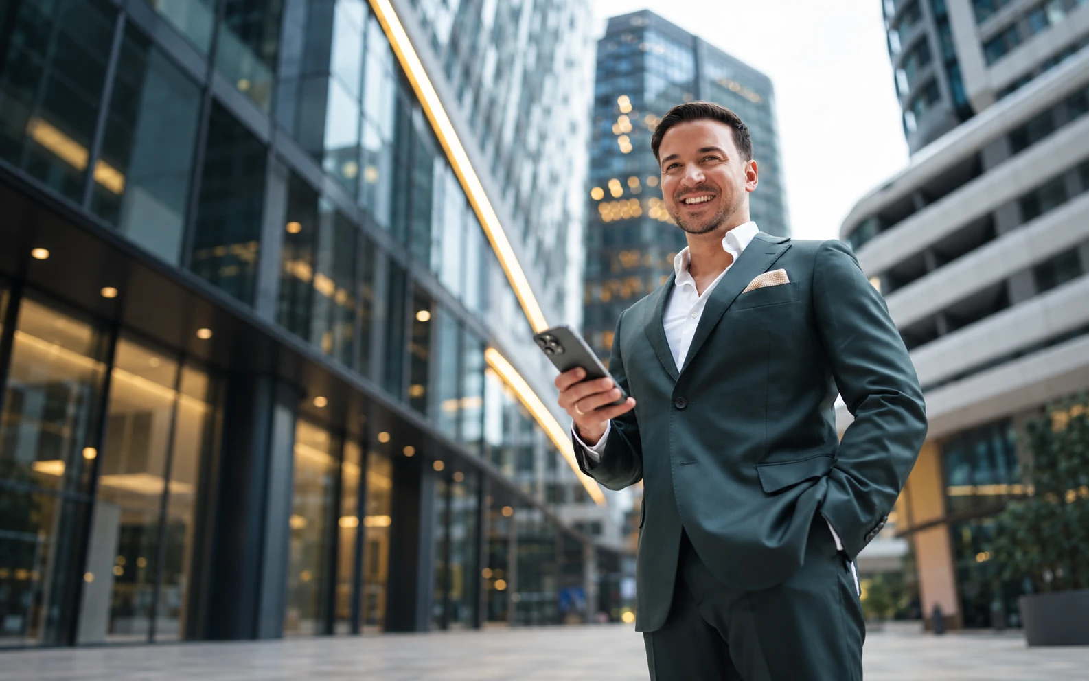 Nikola Andabak mit dem Telefon in der Hand vor moderner Glasarchitektur